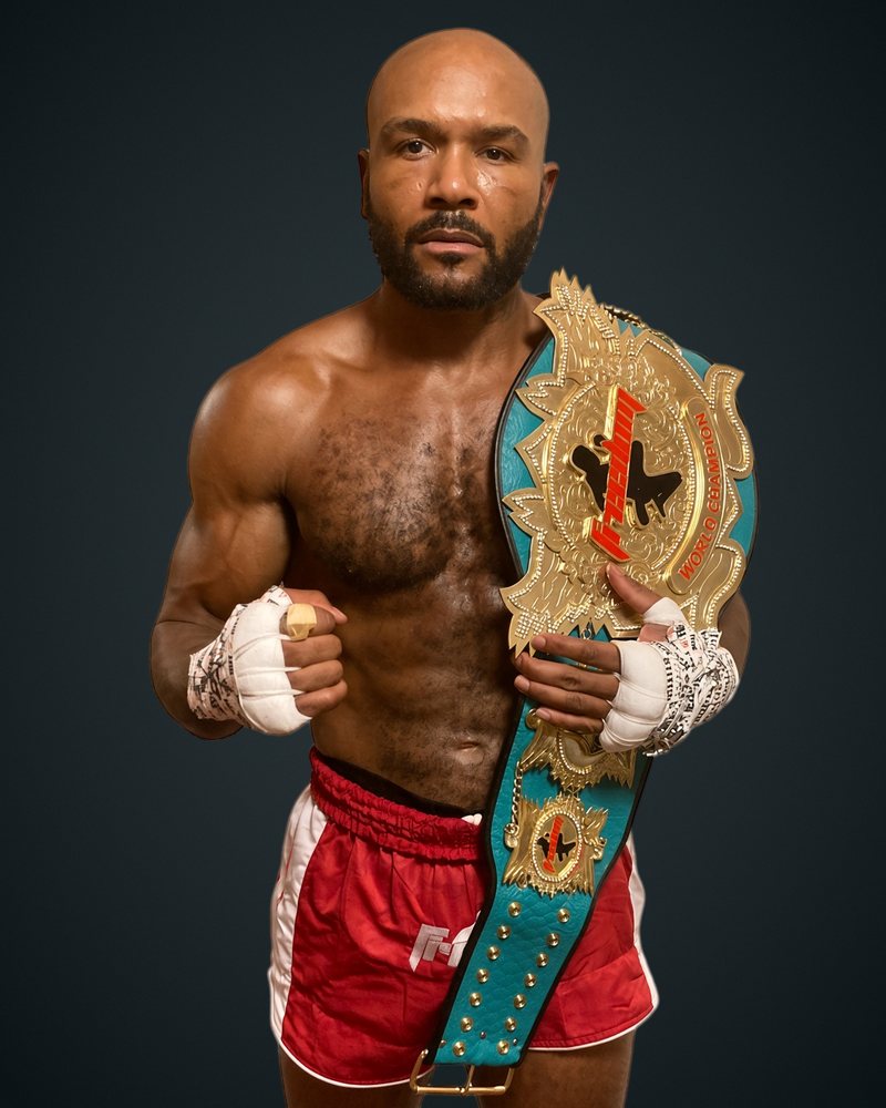 Cyrus Washington holding a championship belt, wearing red Muay Thai shorts and hand wraps